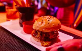 American style burger and chips on a white rectangular platter, scene is a red hued vibrant restaurant